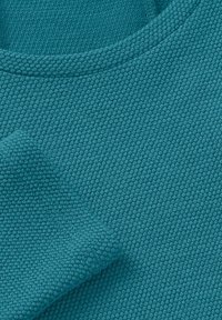 Teal textured fabric with a raised pattern; features a crew neckline and folded cuff. Material appears soft and breathable.