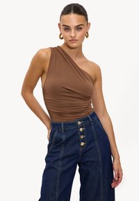 Bodysuit marron à une épaule avec des détails froncés, associé à un pantalon en denim foncé taille haute avec des boutons dorés et des coutures sur mesure.