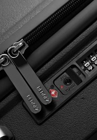 Gros plan sur une fermeture éclair de valise noire avec deux tirettes verrouillées dans un cadenas à combinaison TSA intégré.