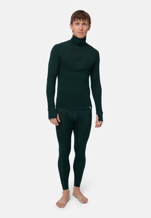 Un homme porte un haut thermique à manches longues vert foncé et un legging assorti sur un fond blanc uni.