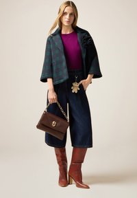 Chaqueta de cuadros en azul marino y verde, blusa morada, pantalones de mezclilla de pierna ancha, bolso marrón con detalles dorados y botas altas marrones con tacón.