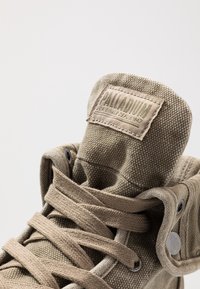 Baskets montantes en toile beige avec une tige en textile, des lacets ronds, des œillets en métal et une languette rembourrée ornée d'une étiquette de marque.