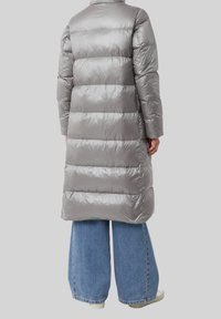 Dikke, lange jas van glanzende grijze stof met horizontale quilt. Kenmerkt zich door lange mouwen en een rechte silhouet, gecombineerd met blauw, wijduitlopende jeans.