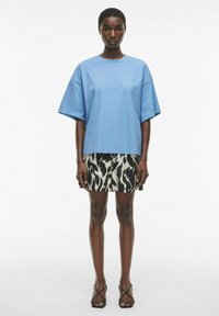 Lys blå oversized bomull t-skjorte med korte ermer, kombinert med et sort og hvitt dyreprint mini skjørt og svarte sandaletter med stropper.