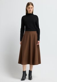 Top negro de mangas largas, falda texturada marrón hasta la rodilla, botas negras de tobillo con punta puntiaguda, superficie lisa y cintura ajustada.