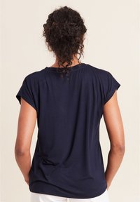 Marineblaues T-Shirt mit kurzen Ärmeln, lockerer Passform, weicher Textur und rundem Ausschnitt. Der glatte Stoff fällt sanft über die Schultern und den Rücken.