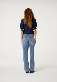Hoog-waisted, lichtblauwe denim jeans met een ontspannen pasvorm, voorzien van twee achterzakken en subtiele slijtage aan de zoom. Gepaard met een marineblauw top.