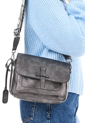 Black textured crossbody bag with a flap closure, adjustable strap, and a prominent front accent. Paired with a light blue knit sweater.
