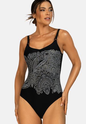 Kobieta ubrana w czarny jednoczęściowy strój kąpielowy z szarymi, skomplikowanymi wzorami paisley i kwiatowymi, z regulowanymi ramiączkami na ramionach, pozująca z ręką na biodrze.