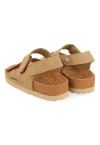 Sandalias de color tostado con correa ajustable, plantilla de corcho y suela de goma texturizada. Presentan un material superior suave y un cierre lateral a presión.