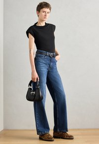 Svart tettsittende topp, høybudde blå denimjeans, sko med leopardmønster, og en svart håndveske med sølvdetaljer. Minimalistisk design og avslappet passform.