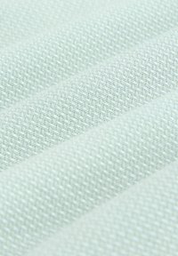 Približnji posnetek svetlo modrega blaga z teksturiranim, tkanim vzorcem in mehke gube, ki tvorijo diagonalne črte.