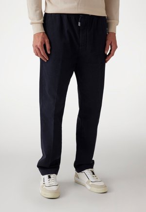 Navy blue elastic-waist trousers made from a soft fabric, featuring a straight-leg design and minimalistic accents. Paired with white sneakers.