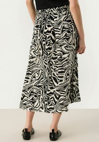 Jupe midi à motif noir et blanc avec un design fluide, une taille élastique et des plis, associée à des chaussures noires brillantes.