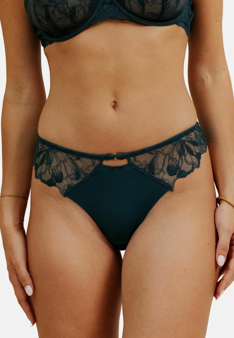 Bikini en dentelle turquoise avec des détails en tulle transparent à la taille, des bords festonnés, un motif floral et une petite accent doré au centre.