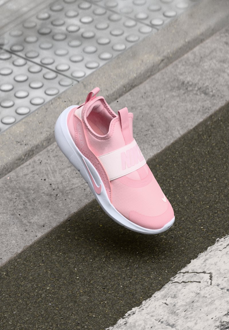 Różowy sneaker Nike z teksturowaną cholewką, elastycznym paskiem i białą podeszwą. Projekt zawiera wyraźne logo oraz pętelkę na pięcie.