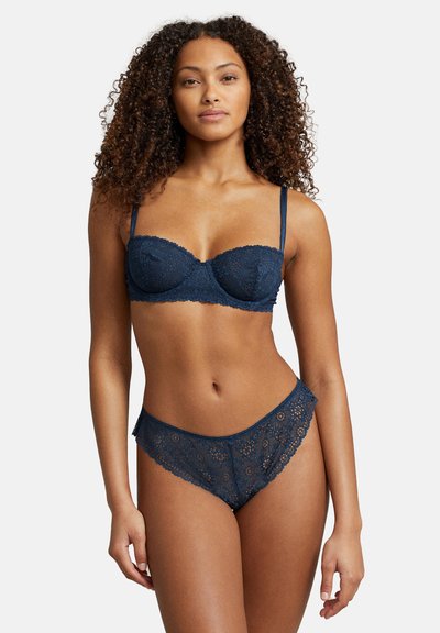 Marinblå spetsunderkläder bestående av en vadderad behå med vågiga kanter och justerbara axelband, tillsammans med matchande spetsunderbyxor.