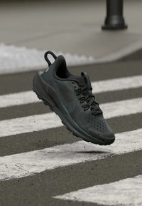 Melns skriešanas apavu modelis ar sietveida virsu, teksturētām sānu paneļiem un mīkstu zoli, ar šņorēšanas aizdari un cilpu.