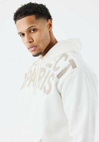 Sudadera blanca de tela suave con gran lettering en beige que dice "PARIS" y detalles en acento. Cuenta con capucha ajustable y bolsillo frontal.