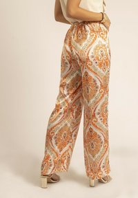 Pantalons large en tissu léger et à motifs, ornés de vives designs en paisley orange, vert et crème, avec une taille élastique.