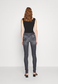 Top negro ajustado combinado con jeans skinny de un gris oscuro que presentan un ligero desgaste. Textura suave con sutiles detalles en los bolsillos traseros.