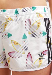 Bílé plavky s vzorem surfovacích prken, zahrnující barvy jako zelená, žlutá a červená. Černé boční pruhy a akcent v podobě loga Adidas.