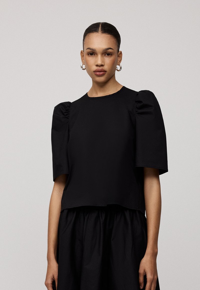 Zwarte cropped top met korte pofmouwen, ronde halslijn en een cropped snit. Gemaakt van een gladde stof, met een minimalistisch ontwerp.
