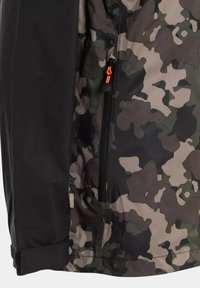 Kamouflagejacka med svart ärm, ficka med zipp och orange dragband, samt en svensk flagga, gjord av texturerat tyg.