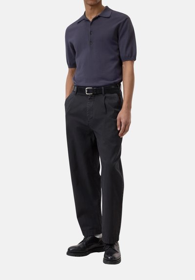 Polo shirt a maniche corte blu navy con colletto, abbinato a pantaloni neri con pieghe e scarpe nere, con una cintura in pelle.