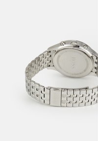 Orologio in acciaio inossidabile silver con cinturino testurizzato, cassa circolare e tre pulsanti. Presenta il logo del marchio inciso sul retro e sulla chiusura.