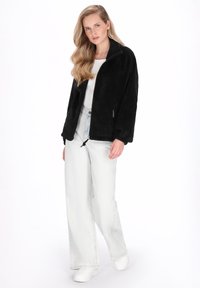 Czarna, puszysta kurtka polarowa z wysokim kołnierzem, zamkiem błyskawicznym i bocznymi kieszeniami, zestawiona z jasnymi dżinsami i białymi trampkami.