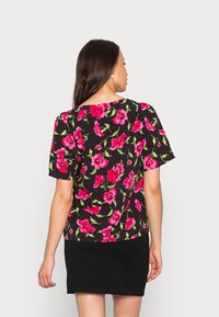 Blusa floral com mangas curtas, apresentando flores cor-de-rosa vibrantes sobre um fundo preto. Tecido suave, corte descontraído e decote redondo.