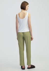 Top bianco senza maniche con schiena a scollo, abbinato a pantaloni dritti leggeri color verde oliva e sandali piatti marroni.
