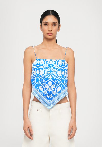 Haut court à motifs bleu et blanc avec de fines bretelles réglables, présentant une forme triangulaire et de grands motifs décoratifs le long des bords.