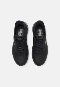 Baskets noires à lacets avec tige en maille, semelle texturée et col rembourré. Présente la marque "SKECHERS GOWALK" à l'intérieur.