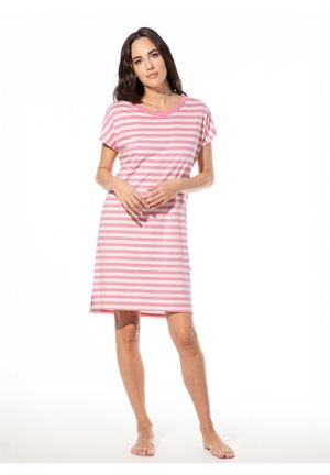 Frau steht barfuß und trägt ein knieumspielendes Kleid mit kurzen Ärmeln in Pink und Weiß gestreift vor weißem Hintergrund