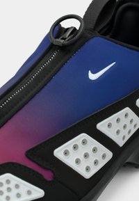 Gros plan d'une sneaker bleu et rose dégradé avec une fermeture éclair noire, un logo Nike blanc et des panneaux de ventilation en caoutchouc blanc sur le côté.