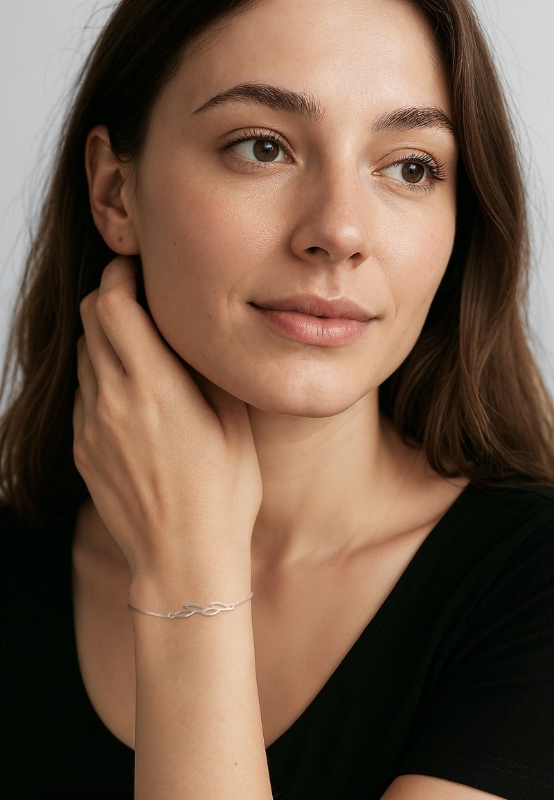 Bracelet en argent avec un design complexe en boucles, porté au poignet, comportant une fine chaîne et une finition lisse et polie.