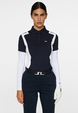 Polo navy con accenti bianchi, colletto e logo; abbinato a pantaloni scuri e una cintura nera con fibbia argento; guanto da golf bianco.