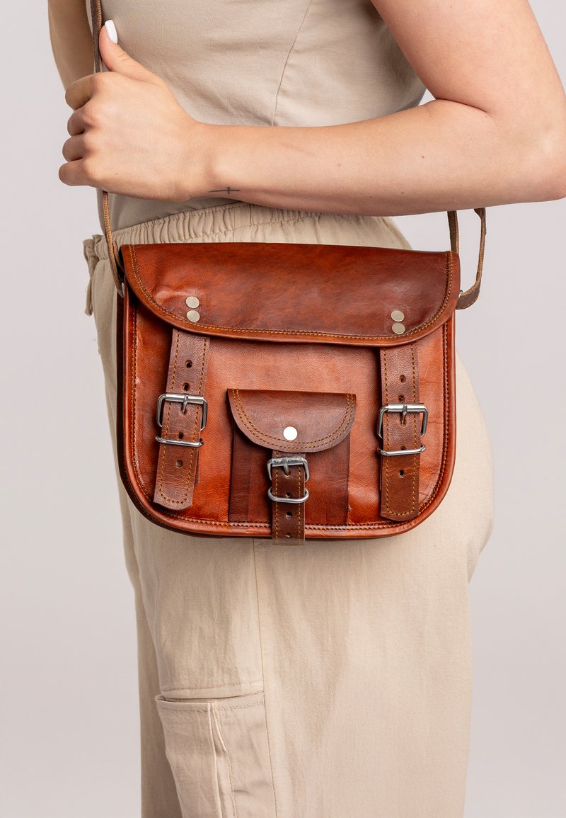 Hnedá kožená crossbody taška s klopou, nastaviteľným popruhom, dvoma prednými prackami a malou prednou kapsou. Hladký povrch so striebornými akcentmi.