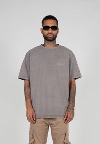 Gray cotton oversized t-shirt with short sleeves, featuring a light logo on the chest and a relaxed fit. Worn with khaki cargo pants.