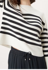 Pull-over en maille côtelée à rayures noires et blanches avec une coupe courte. Caracterisé par un col montant et une coupe décontractée. Associé à un pantalon noir avec cordon de serrage.