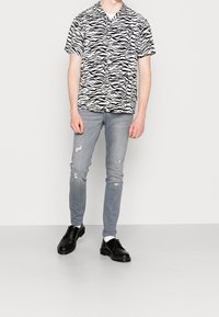 Camicetta a maniche corte a righe zebra bianco e nero abbinata a jeans chiari strappati e scarpe nere stringate.