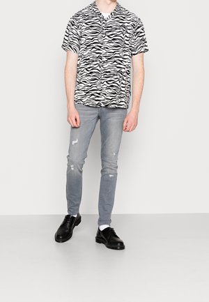 Black and white zebra-striped short-sleeve shirt paired with light blue distressed jeans and black lace-up shoes.