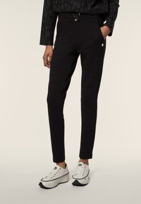 Pantaloni jogger neri realizzati in tessuto morbido, con vita regolabile con cordoncino, tasche laterali e cuciture a contrasto. Abbinati a scarpe da ginnastica bianche.