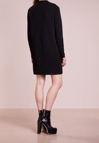 Abito nero a maniche lunghe realizzato in tessuto knit, con taglio dritto. Abbinato a stivali neri in pelle con plateau e chiusura con zip.