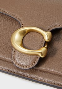 Braune Lederhandtasche mit strukturierter Oberfläche, ausgestattet mit einem goldenen runden Verschluss und kontrastierenden Nähten entlang der Kanten.