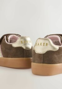 Brūnas zamša sporta kedas ar teksturētu zelta papēdi un rozā odere. Sānos ir rozā un bēša austs raksts. Brūna gumijas zole.