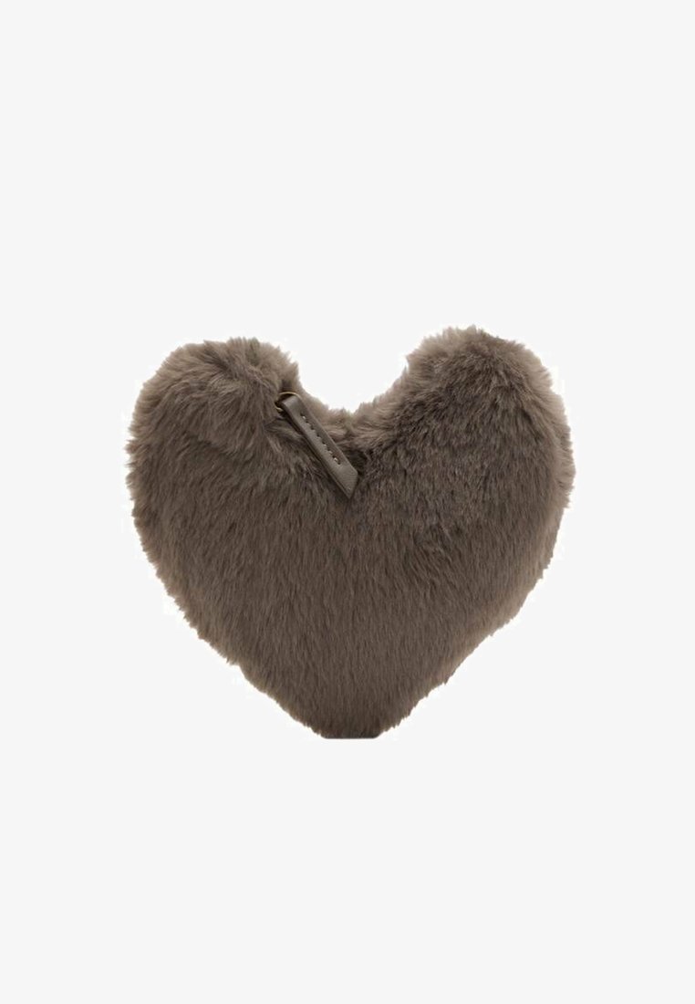 Coussin en forme de cœur en fausse fourrure grise douce, avec une surface texturée et une petite étiquette en tissu sur un côté.