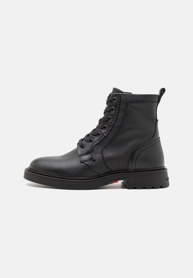 Bottine noire en cuir avec lacets à l’avant, languette au talon et semelle robuste avec un petit détail rouge, blanc et bleu.